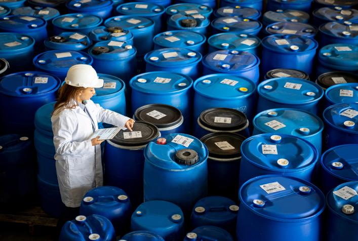 worker in a sea of blue chemical storage barrels 