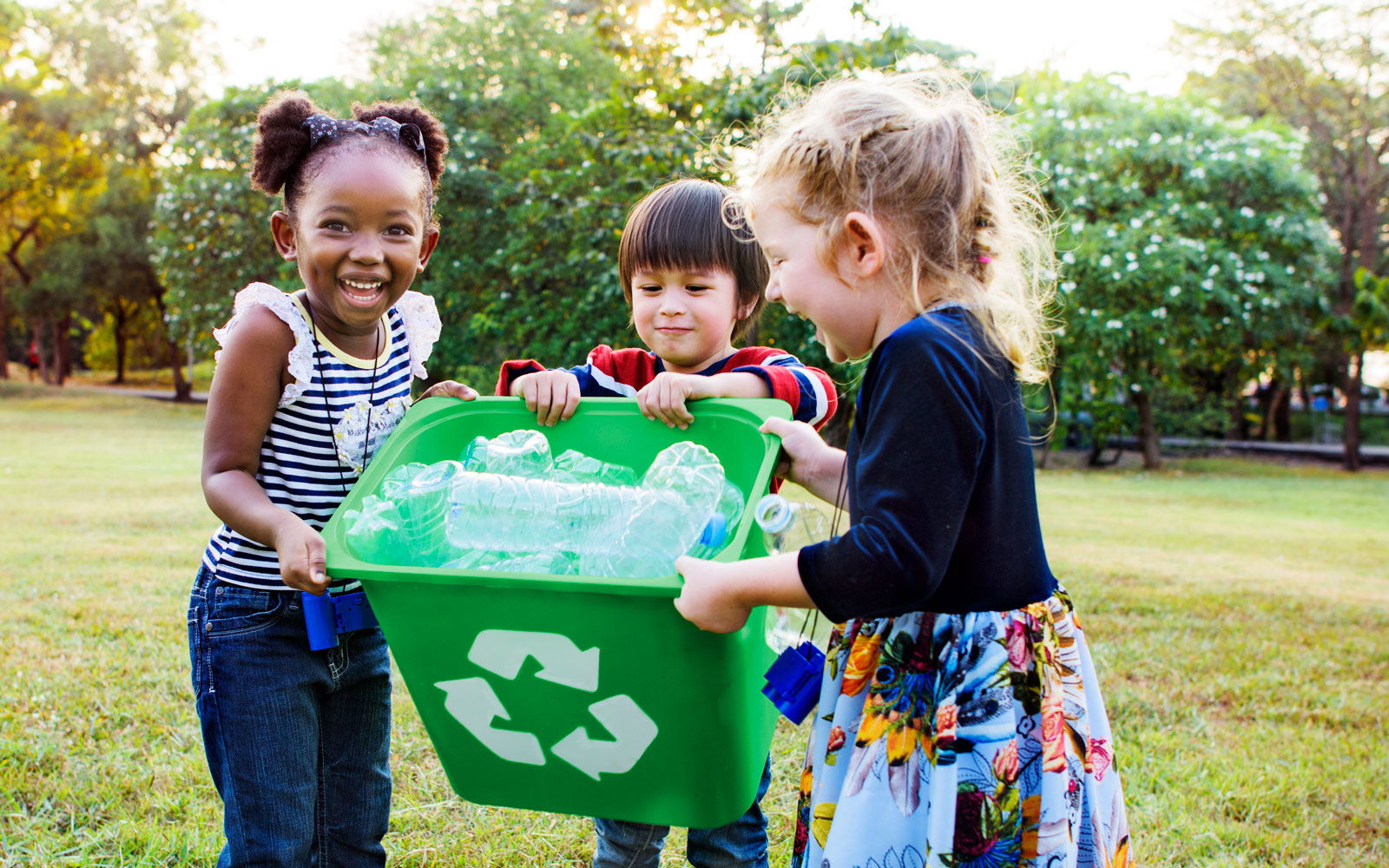 Three children holding a green recycling bin full of plastic bottles