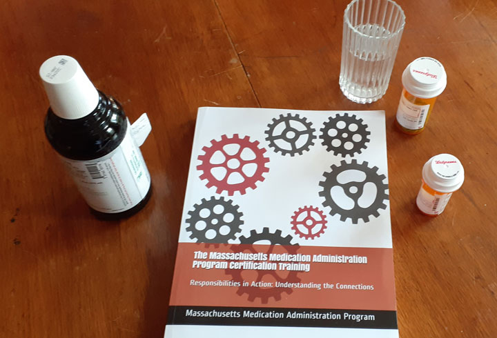 photo of training manual on a table along with bottles of medication and a glass of water