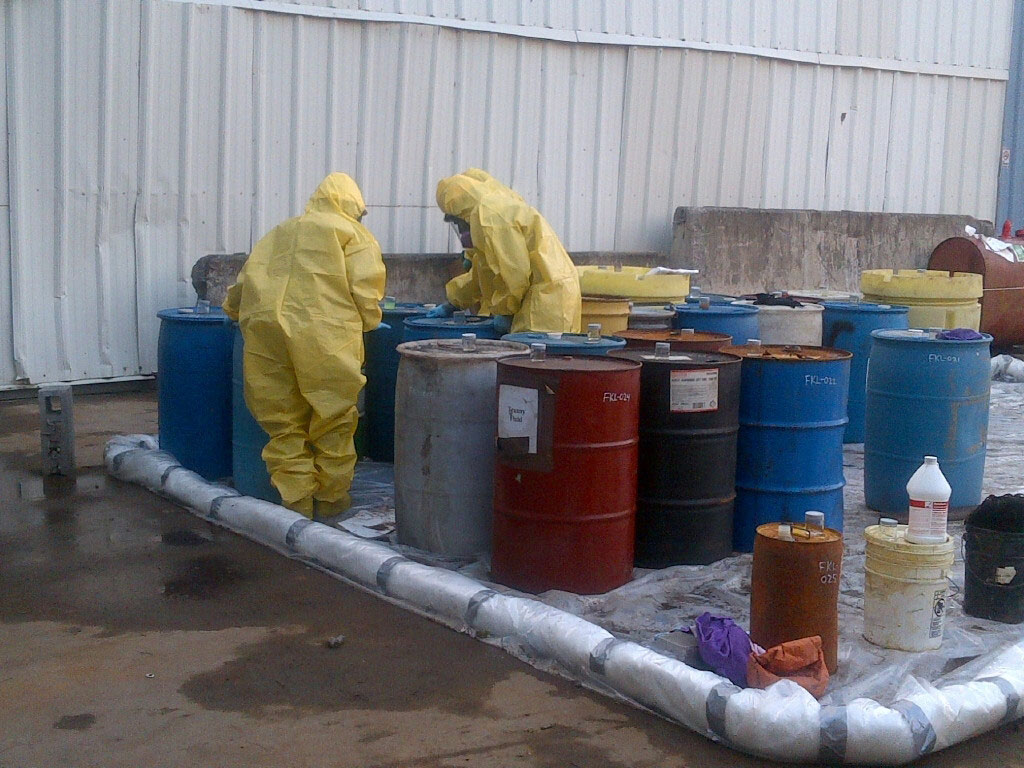 Photo of people in yellow protection suits over contamination barrels