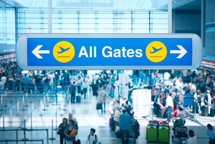 Photo of a busy airport terminal with directional signs to the gates