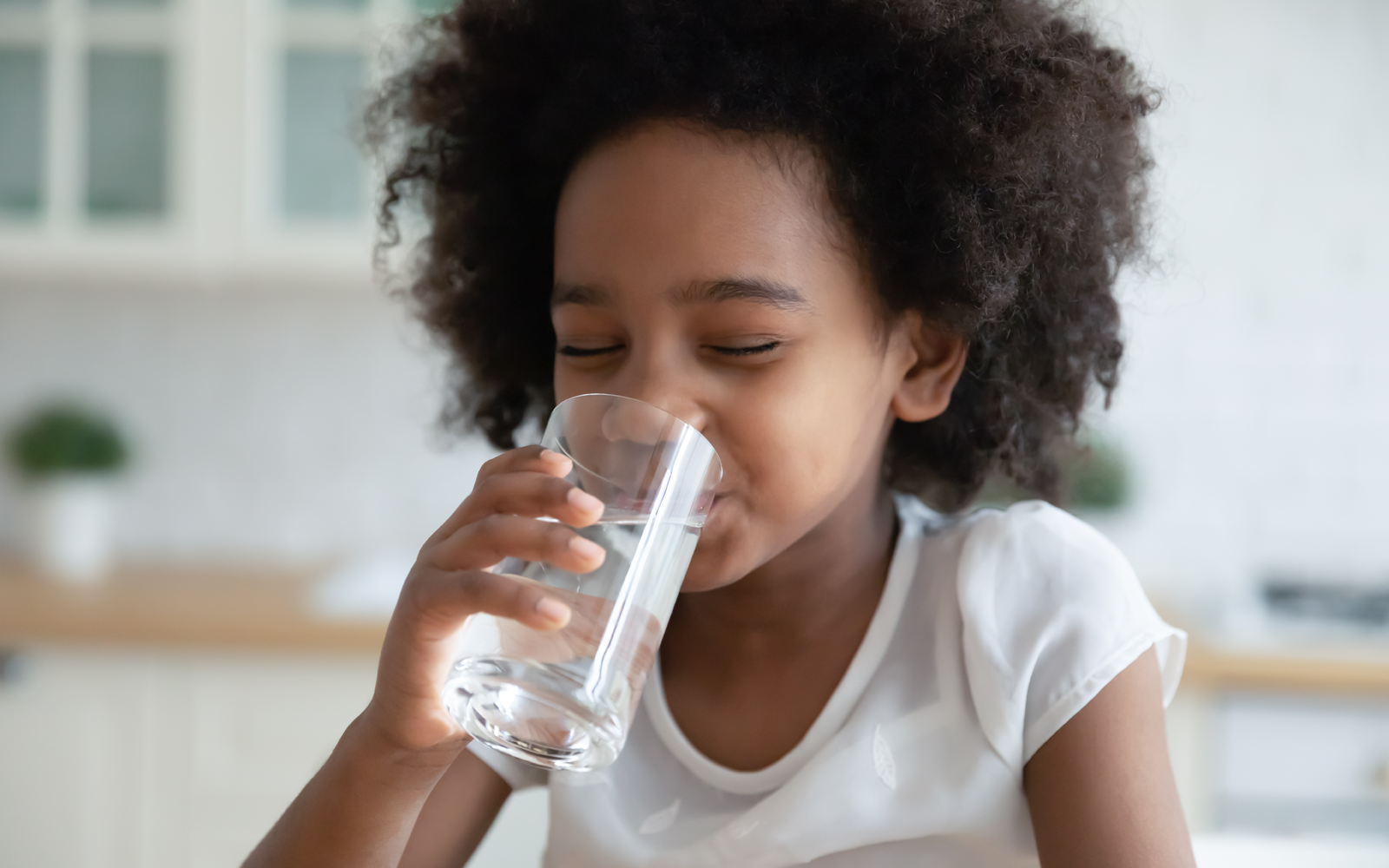 Young African American girl drinks a glass of clean water in kitchen