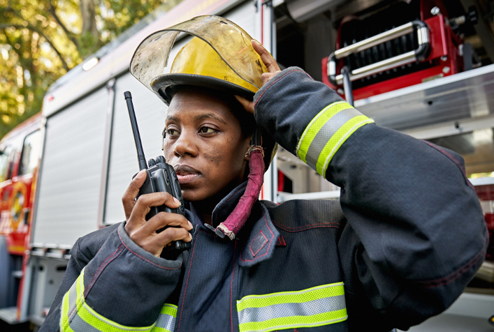 Photo of a person wearing firefighting gear speaking into a handheld radio