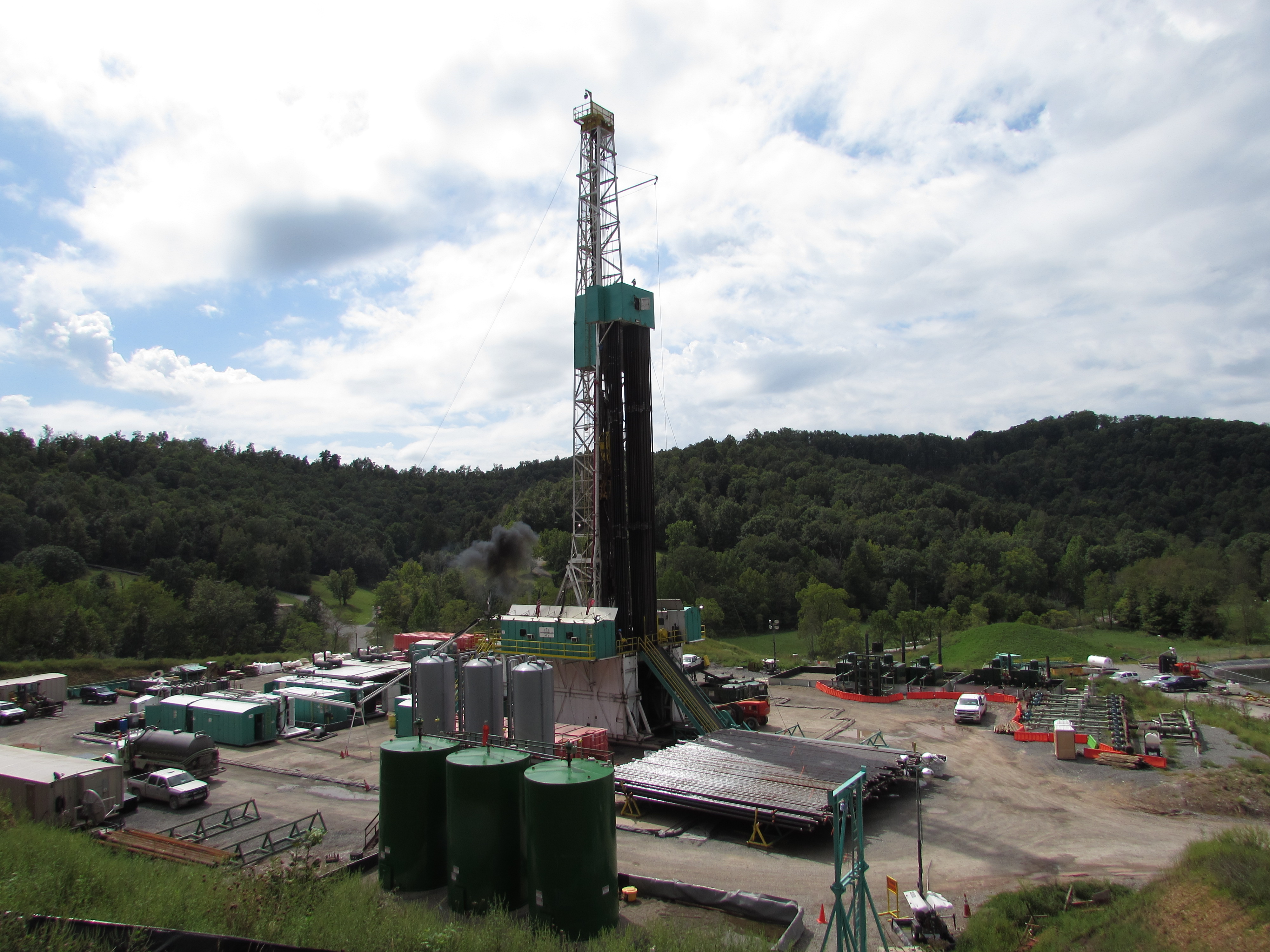 A drilling rig stands prominently in a vast field, surrounded by open land and clear skies, showcasing industrial activity.