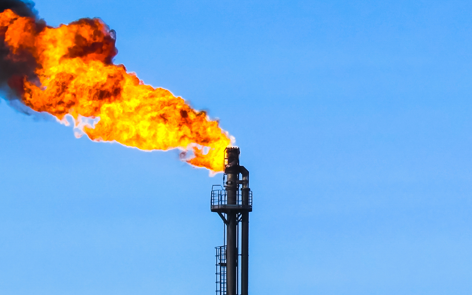 A gas flare illuminates the night sky, casting a bright glow against the dark backdrop of clouds.