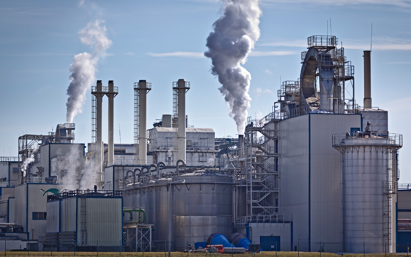 Chemical plant with vapor or smoke plumes rising into the clear blue sky