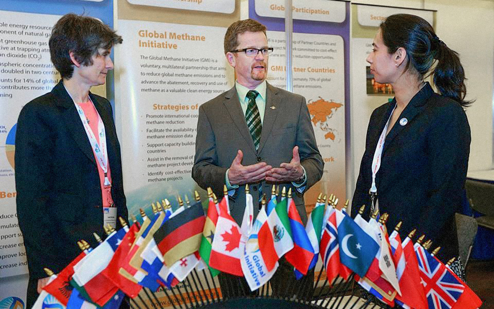 Three professionals stand and talk in front of a poster display about the Global Methane Initiative