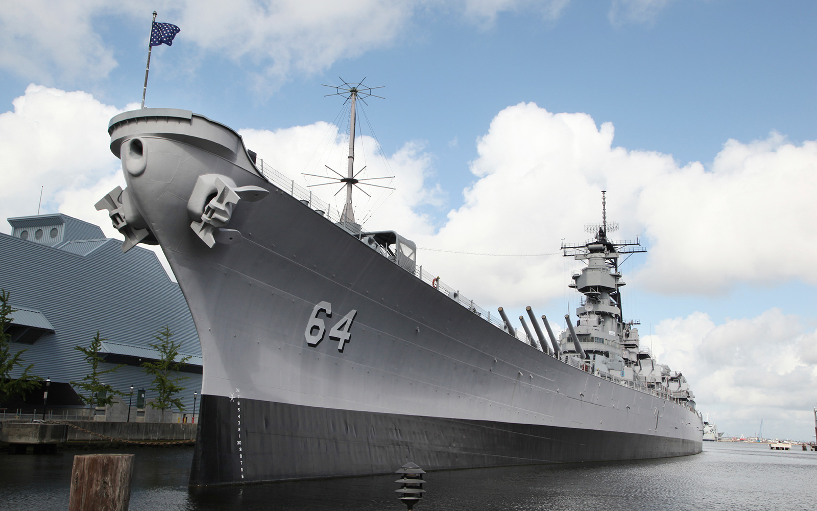 Large Navy battleship sitting dockside in water below a blue sky