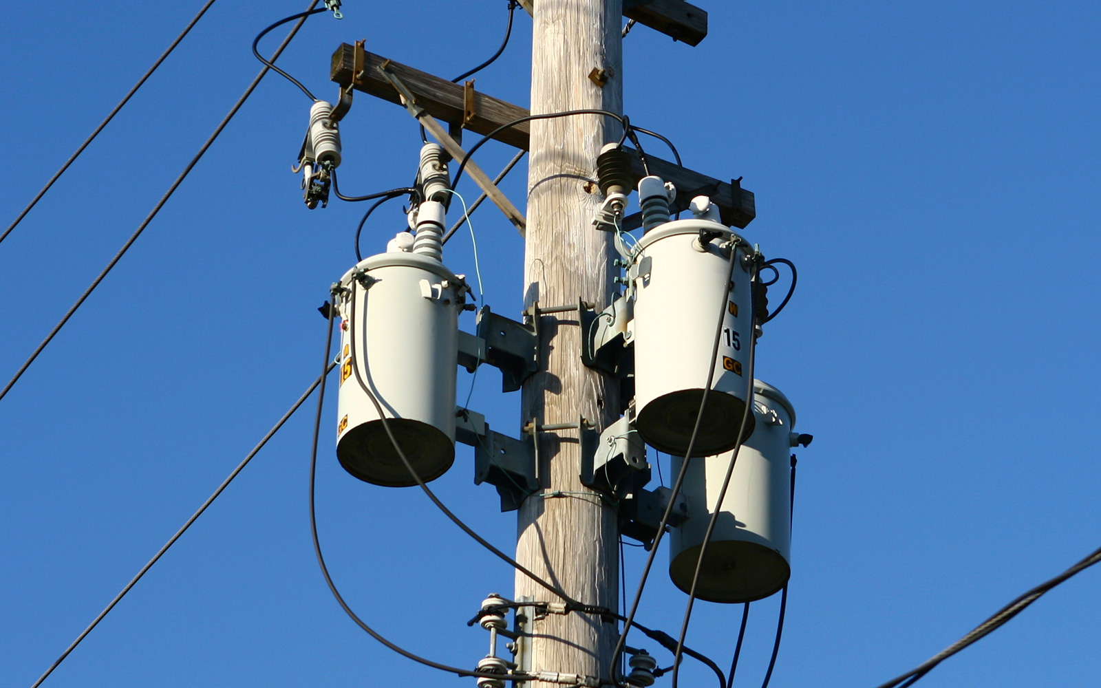 Three cylindrical power transformers suspended atop a utility pole