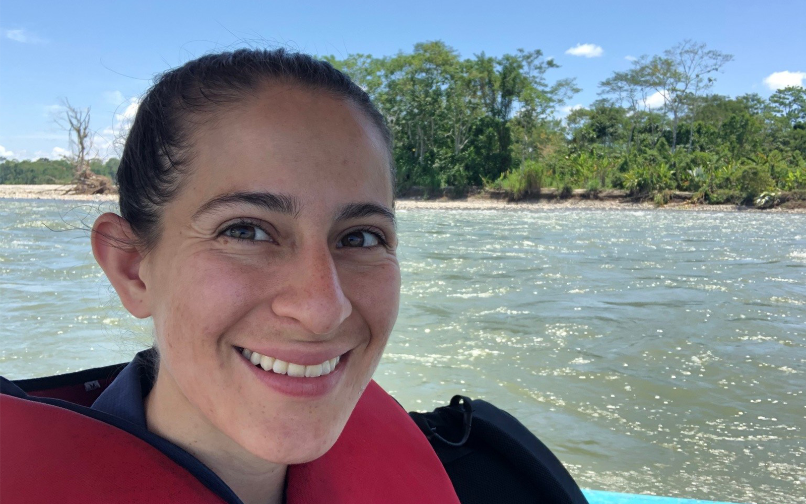 A woman in a life vest, Andrea Cristina Ruiz, smiles in front of the Amazon river